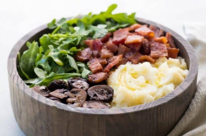 wooden bowl holding an AIP breakfast of mashed cauliflower, sauteed mushrooms, bacon, and arugula.