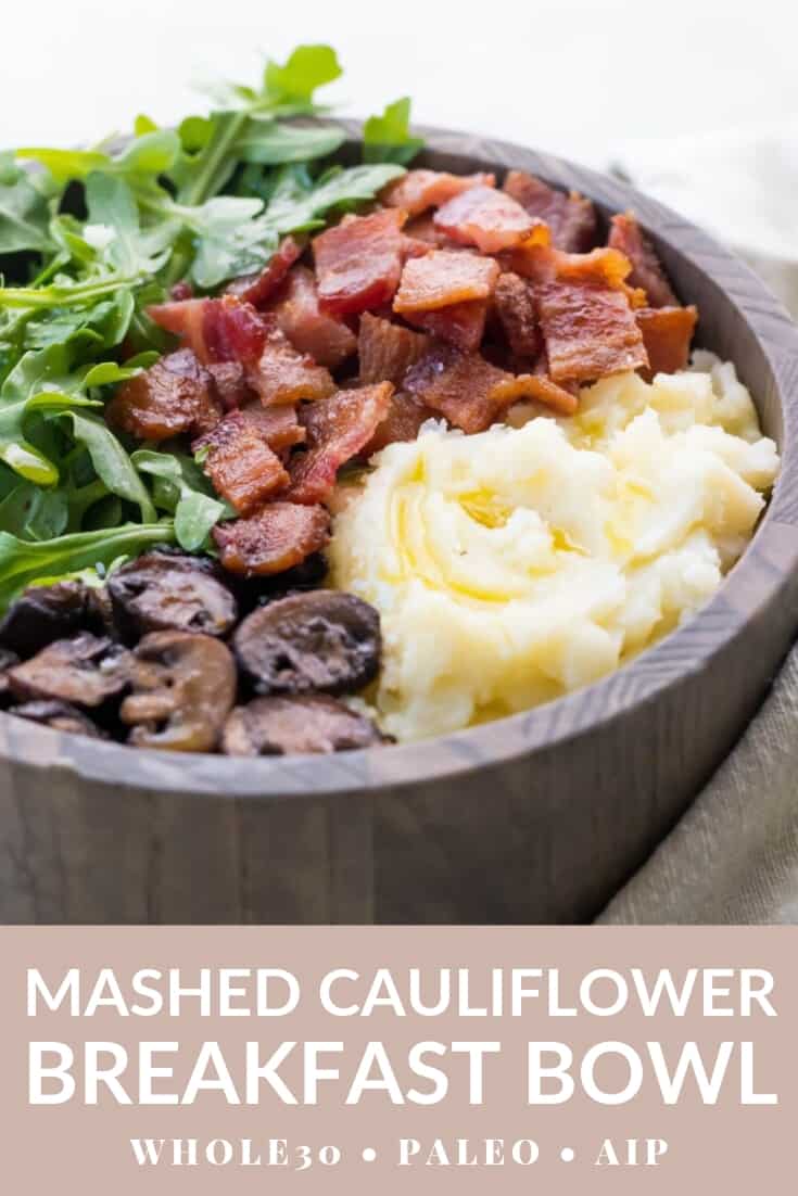 wooden bowl holding an a Whole30 breakfast of mashed cauliflower, sauteed mushrooms, bacon, and arugula. Pink label at the bottom with white text reads: Mashed Cauliflower Breakfast Bowl, Whole30, Paleo, AIP.