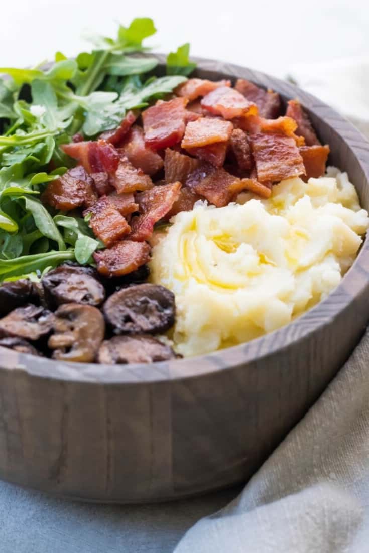 wooden bowl holding an AIP breakfast of mashed cauliflower, sauteed mushrooms, bacon, and arugula.