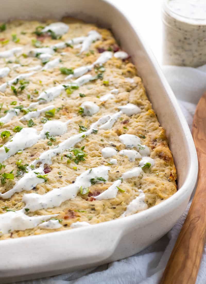 White stoneware casserole dish with a paleo Bacon Chicken Ranch casserole and a wooden spoon