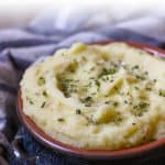 A wood table with a blue bowl of creamy and easy Whole30 Mashed Potatoes cooked in the Instant Pot. These are dairy-free, Paleo, AIP friendly!