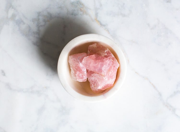 a small bowl of rose quartz healing crystal on a marble background surface