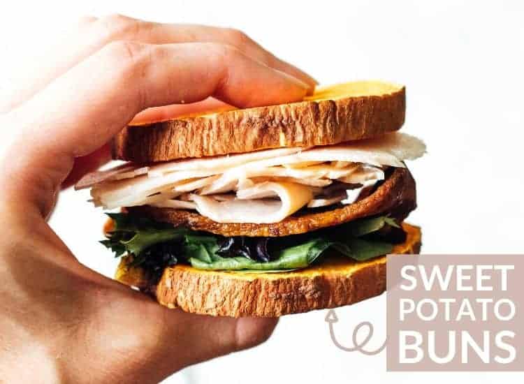 A hand holds a turkey sandwich with bacon and lettuce on a sweet potato bun.