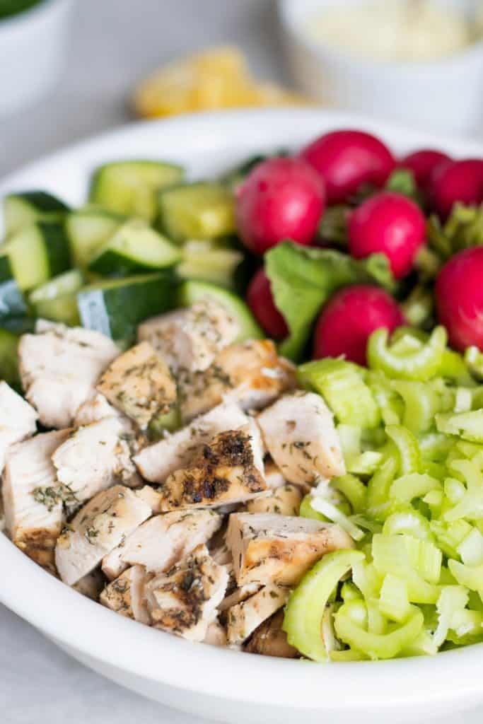 white bowl of whole30 Chicken Salad ingredients like cucumber, radishes, celery, and chicken