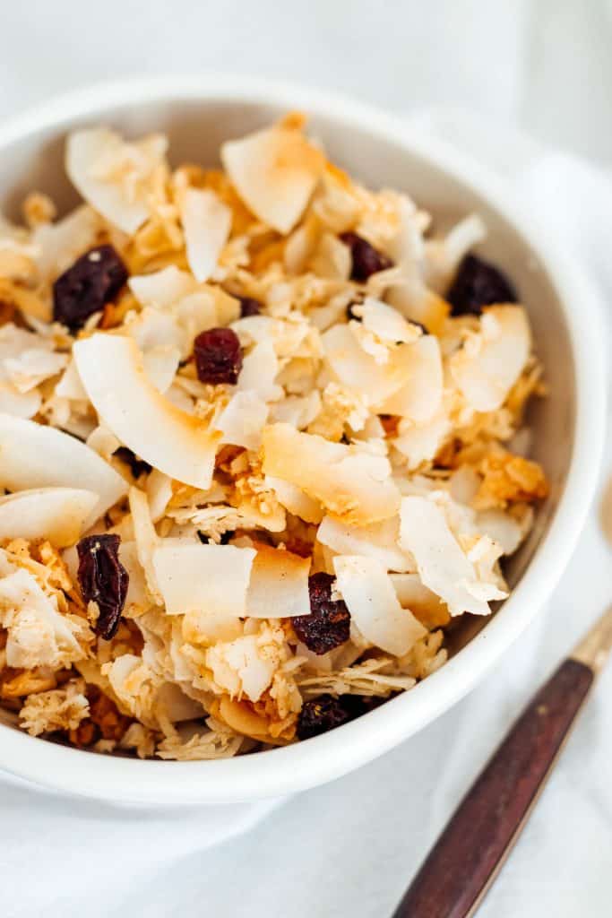 A white bowl full of coconut, nut free, Paleo Granola Cereal with raisins and a gold spoon.