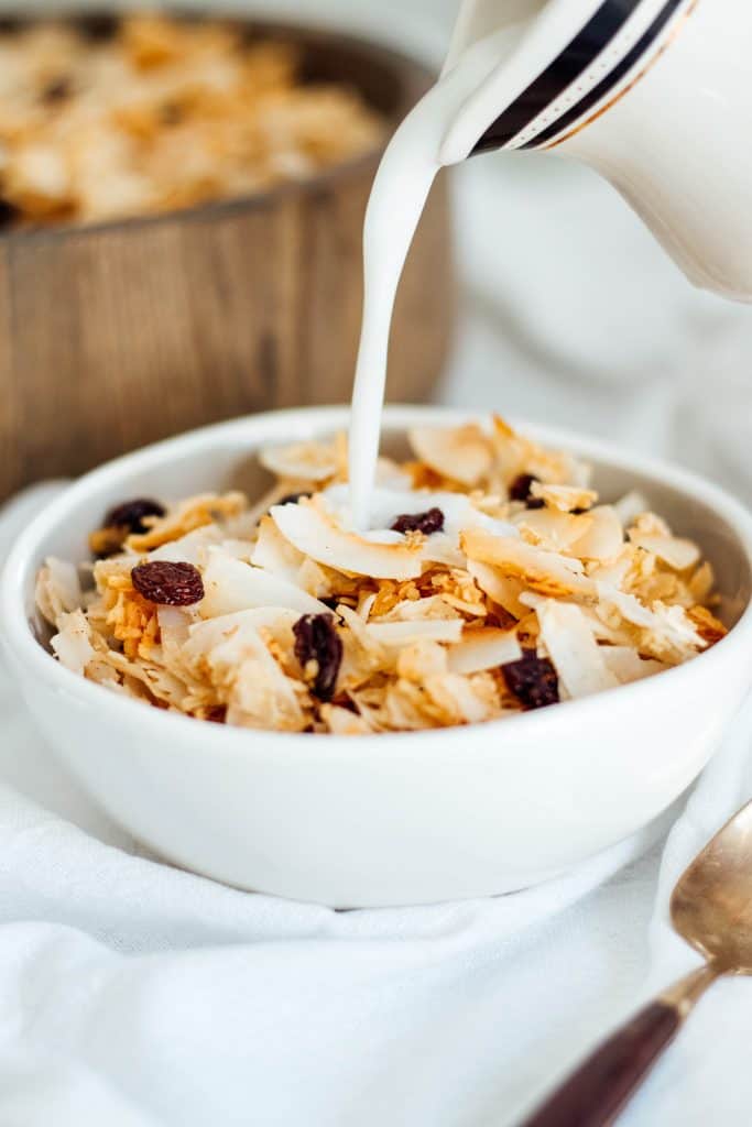 A white bowl of Paleo Granola with cinnamon and raisins with milk being poured on top.