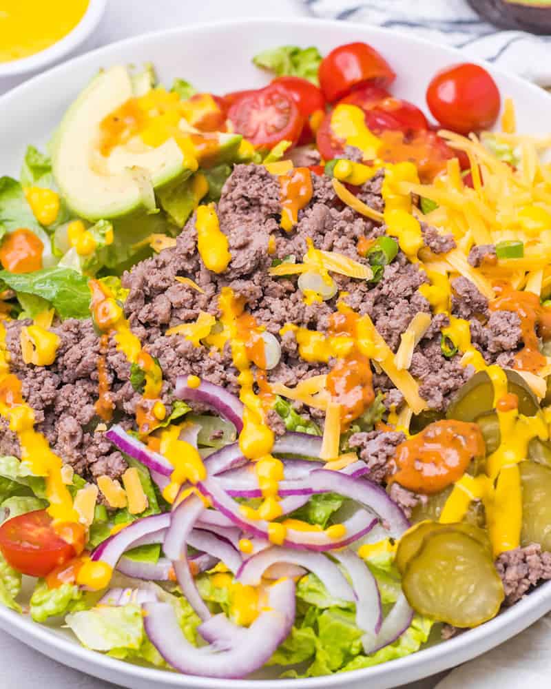 A burger bowl with cheese, dressing, and ground beef on a marble table.