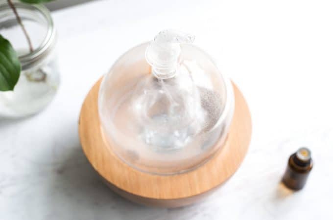 glass and wood diffuser on a white table with an essential oil bottle