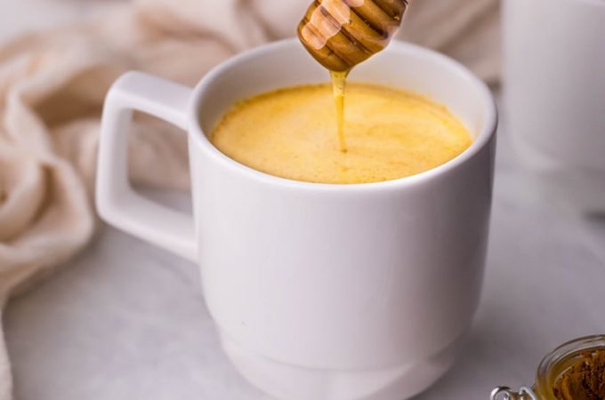 White mug full of turmeric coffee on a white counter with a honey drizzle.