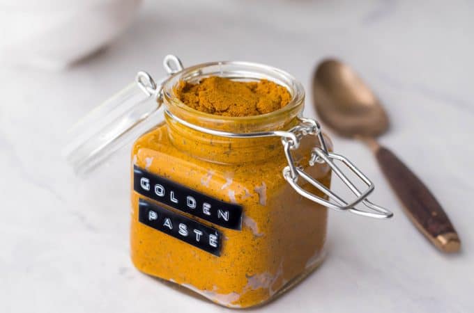 Glass jar full of turmeric paste on a white counter with a golden spoon next to it.