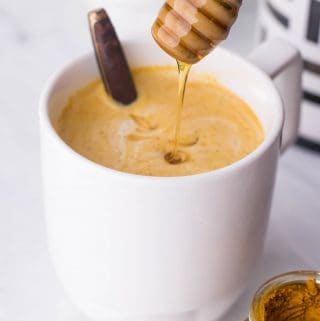 White mug of Turmeric Coffee with honey drizzling into it