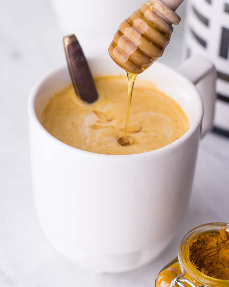 White mug full of turmeric coffee on a white counter with a honey drizzle.
