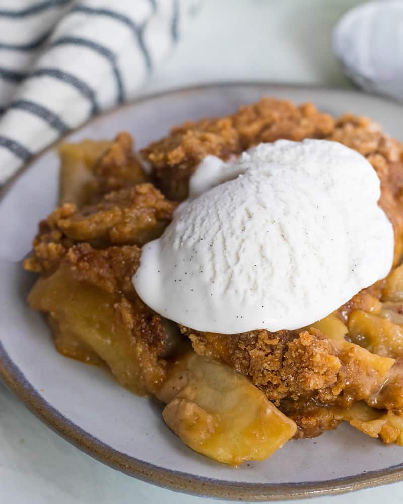 A marble table with a plate of Paleo Apple Crisp and dairy free coconut milk ice cream on top. 