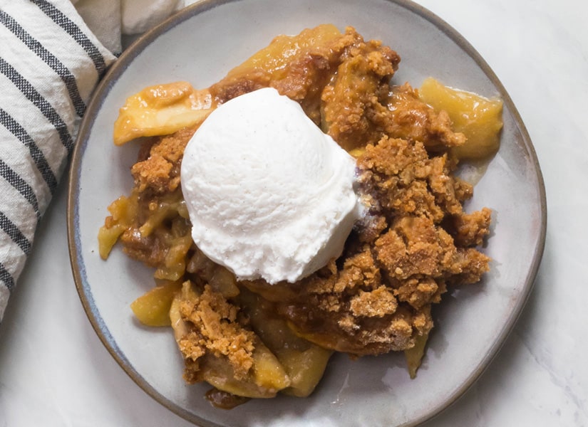 A marble table with a plate of Paleo Apple Crisp and dairy free coconut milk ice cream on top.