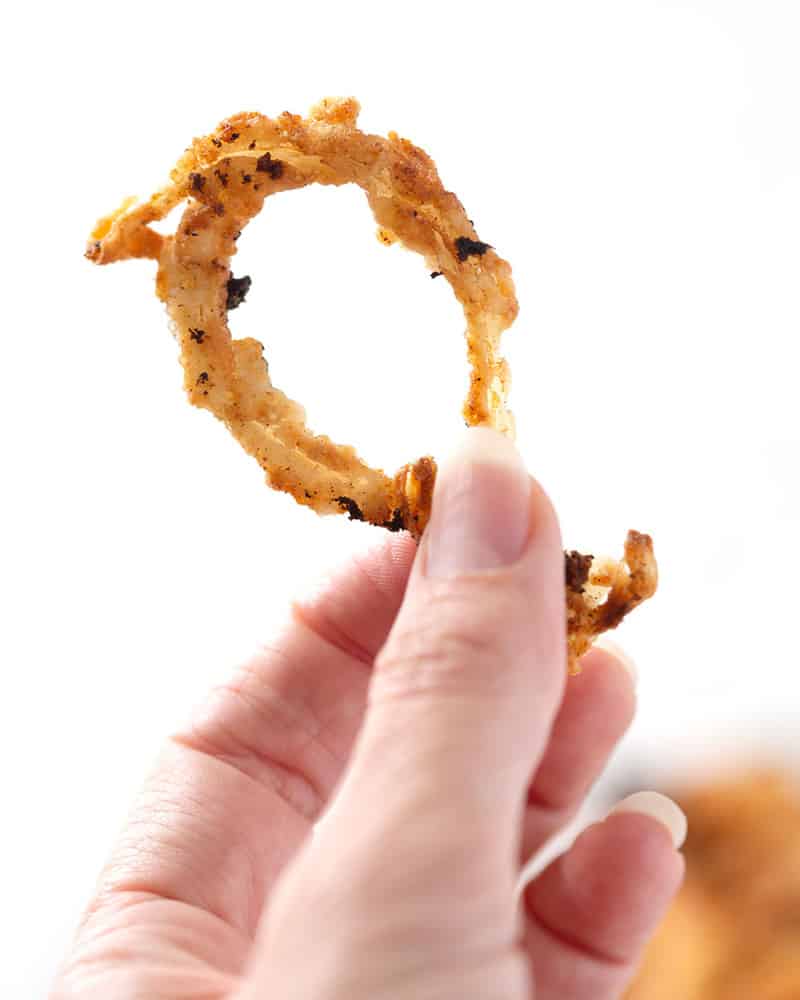 A hand holding a gluten free french fried onion ring in front of a white background.