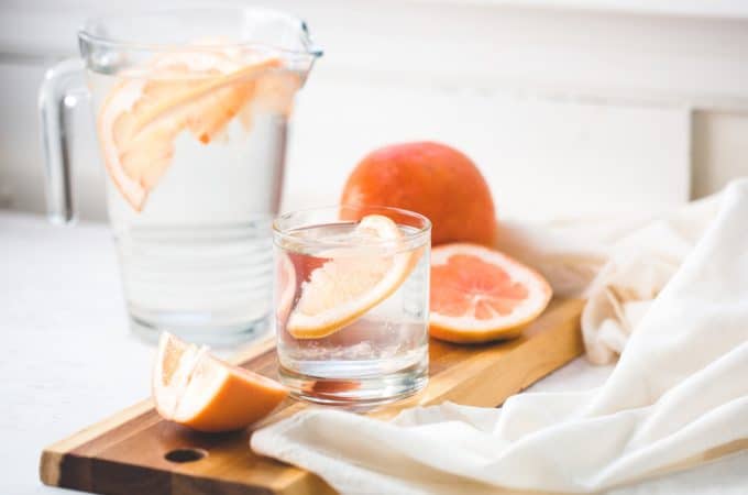 An image of a water jug with grapefruit it in on a marble surface.