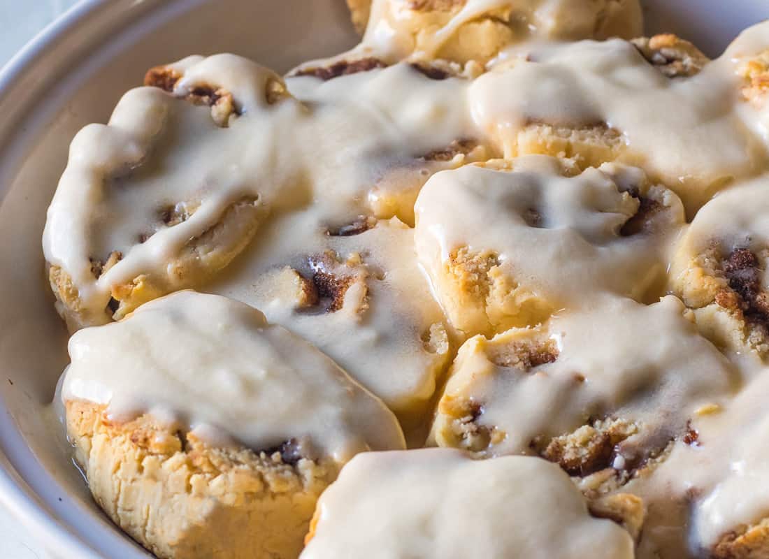 A pie pan of gluten free and paleo cinnamon rolls covered in warm frosting.