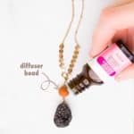 a drop of essential oil is being added to the terracotta stone on an essential oil diffuser necklace laying on a marble table. Under the image, there is text that reads: easy diy essential oil diffuser necklace.