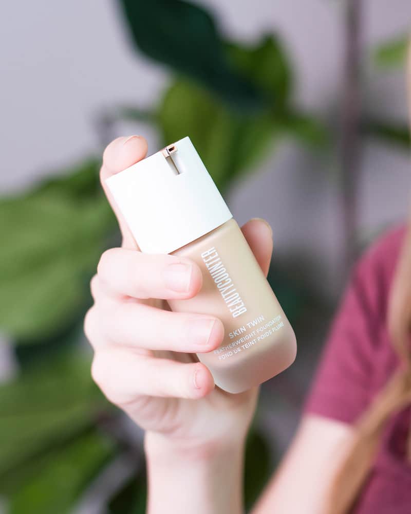 A woman in a pink shirt holds a jar of Beautycounter's Skin Twin foundation. 