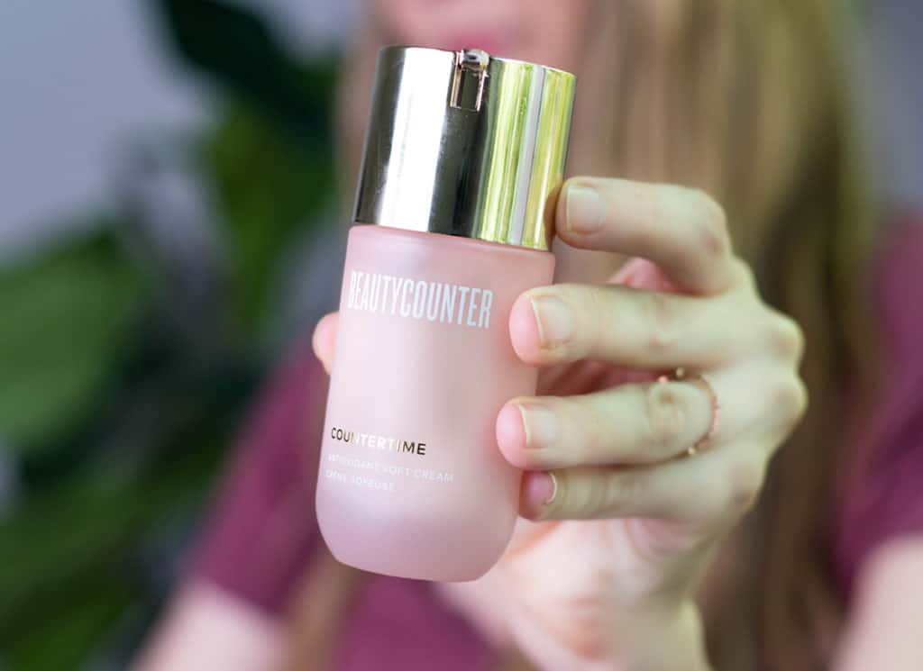 A woman in a pink shirt holds a jar of Beautycounter's Countertime Antioxidant Soft Cream. 