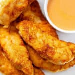 A close up image of whole30 buffalo chicken tenders on a white plate with a ramakin of buffalo dipping sauce.