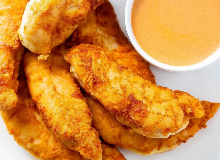 A close up image of whole30 buffalo chicken tenders on a white plate with a ramakin of buffalo dipping sauce.