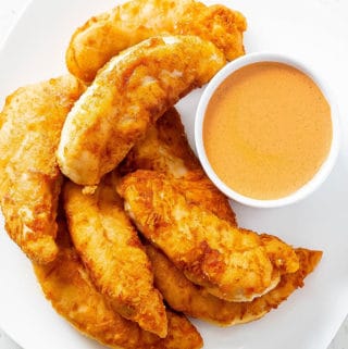 Buffalo chicken tenders on a white plate with a ramakin of buffalo dipping sauce.