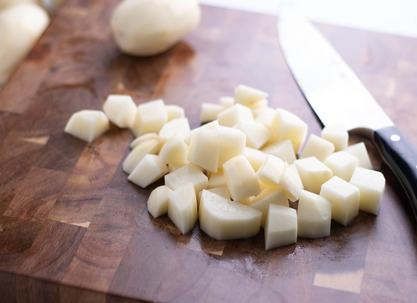 A wooden cutting board with a handful of cubed potatoes.